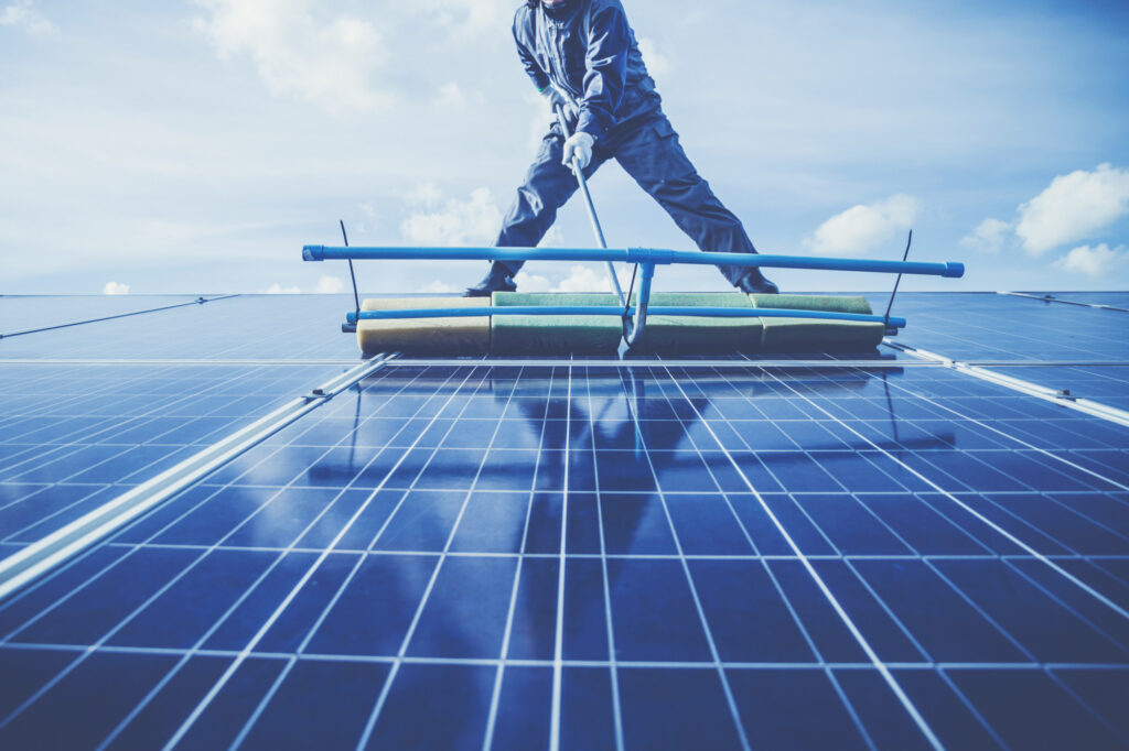 Eine Person reinigt mit einer großen Bürste die Oberfläche einer Photovoltaikanlage.